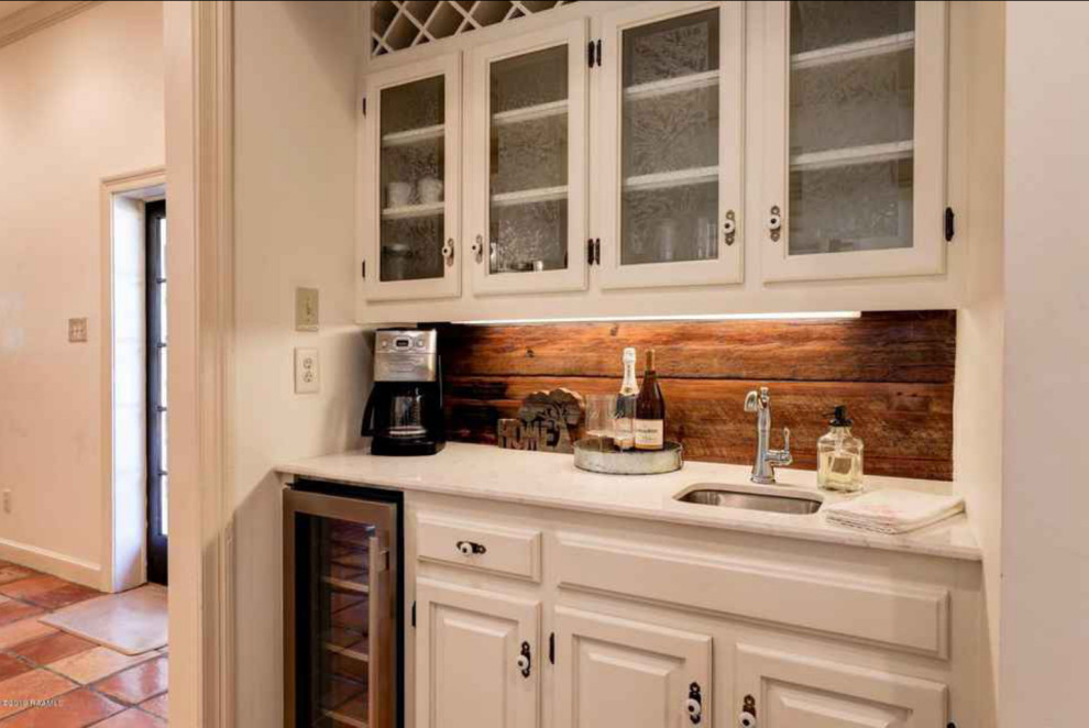 Photo of a country single-wall wet bar in Dallas with an undermount sink, raised-panel cabinets, white cabinets, quartzite benchtops, timber splashback, terra-cotta floors, white benchtop and brown splashback.