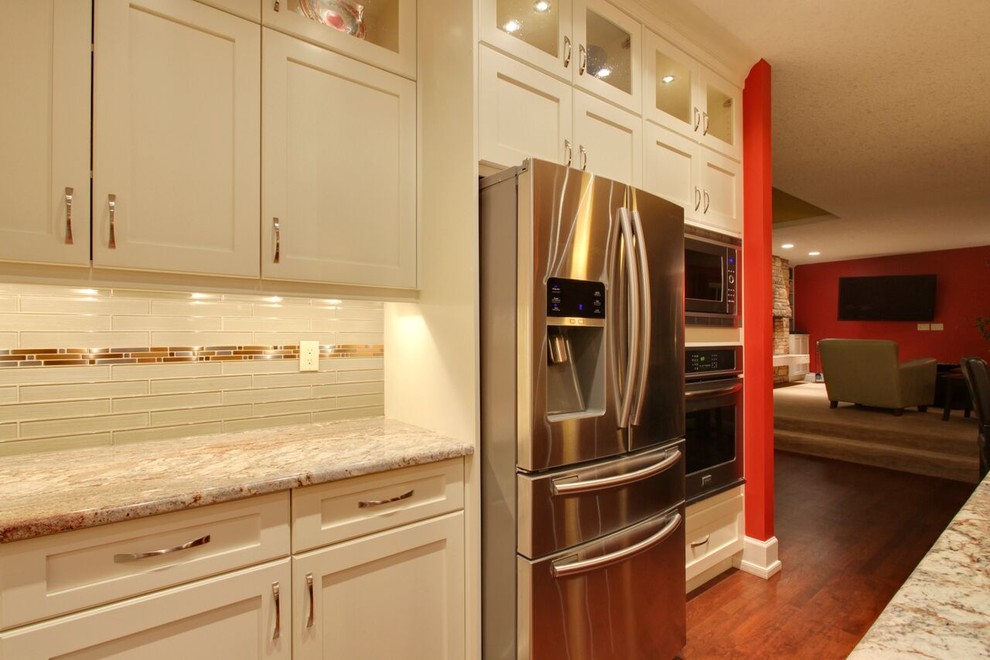 Inspiration for a large transitional l-shaped medium tone wood floor and brown floor open concept kitchen remodel in Calgary with an undermount sink, recessed-panel cabinets, white cabinets, glass countertops, beige backsplash, matchstick tile backsplash, stainless steel appliances and an island