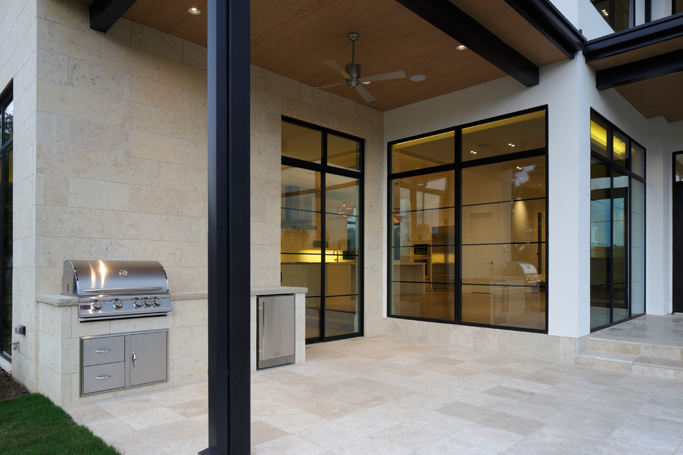 This is an example of a large modern backyard patio in Dallas with an outdoor kitchen, tile and a roof extension.