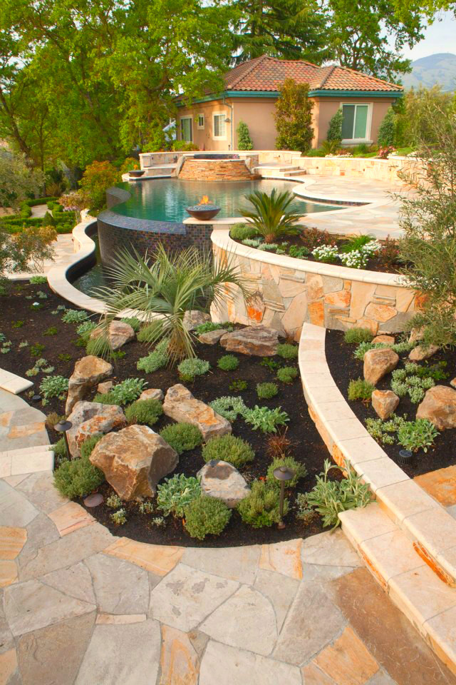 Photo of a large mediterranean backyard full sun formal garden for spring in San Francisco with natural stone pavers and a water feature.