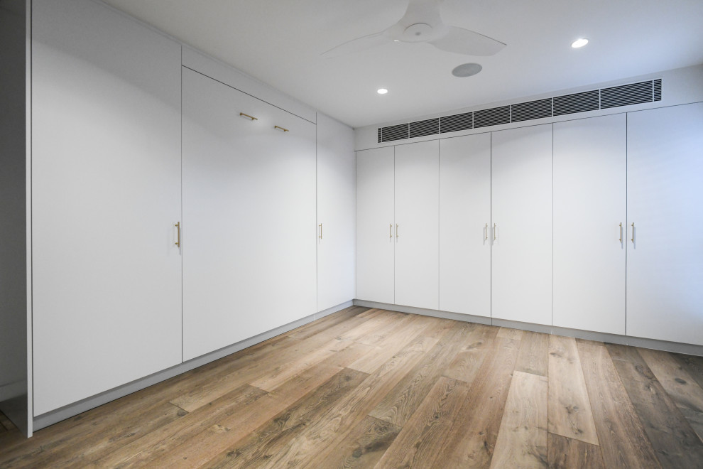 Modelo de despacho minimalista grande sin chimenea con paredes blancas, suelo de madera oscura, escritorio empotrado, suelo marrón y bandeja