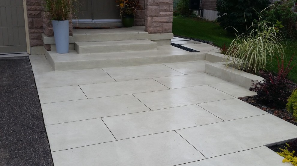 This is an example of a contemporary front yard driveway in Toronto with a retaining wall and concrete pavers.