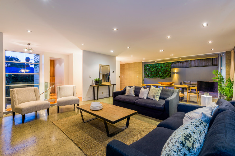 This is an example of a large transitional open concept living room in Auckland with white walls, concrete floors, a standard fireplace and a metal fireplace surround.