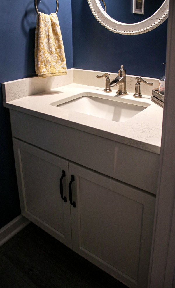 Bild på ett litet vintage vit vitt toalett, med släta luckor, vita skåp, blå väggar, mellanmörkt trägolv, bänkskiva i kvarts och brunt golv