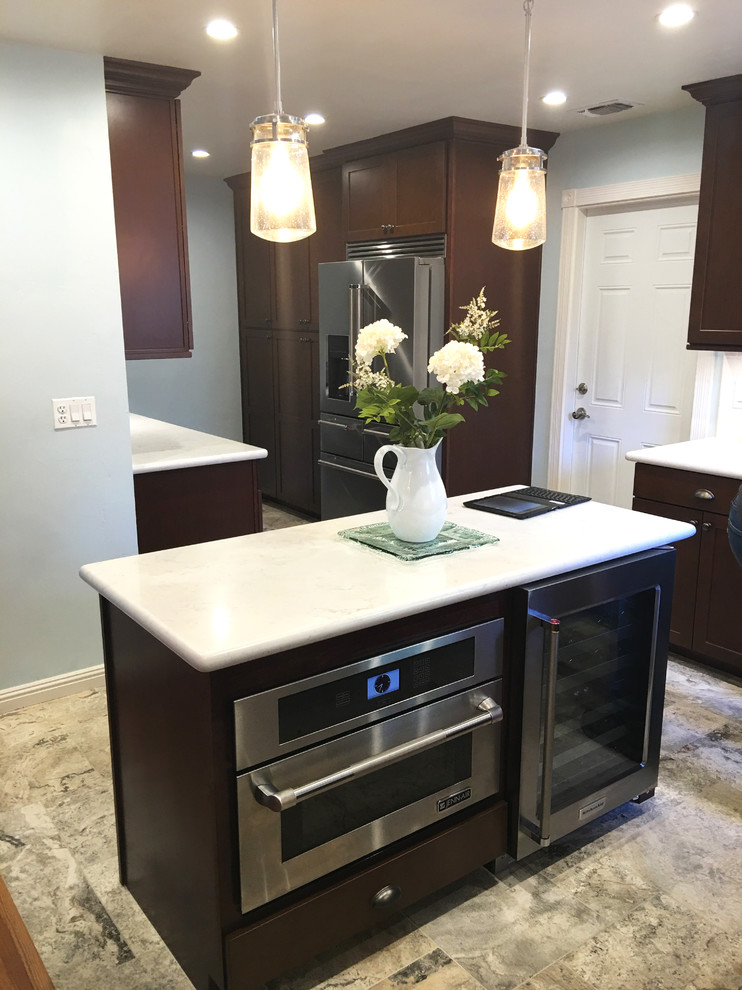 Example of a transitional gray floor kitchen design with shaker cabinets, dark wood cabinets, quartzite countertops, white backsplash, stainless steel appliances and an island