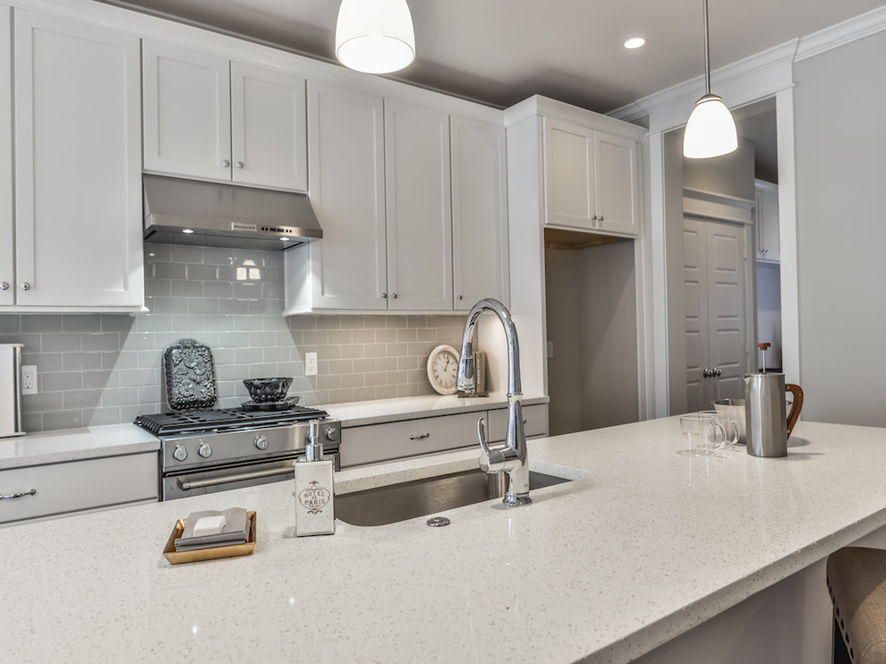 Inspiration for a mid-sized transitional galley open plan kitchen in Houston with an undermount sink, shaker cabinets, white cabinets, quartz benchtops, grey splashback, subway tile splashback, stainless steel appliances, medium hardwood floors and with island.