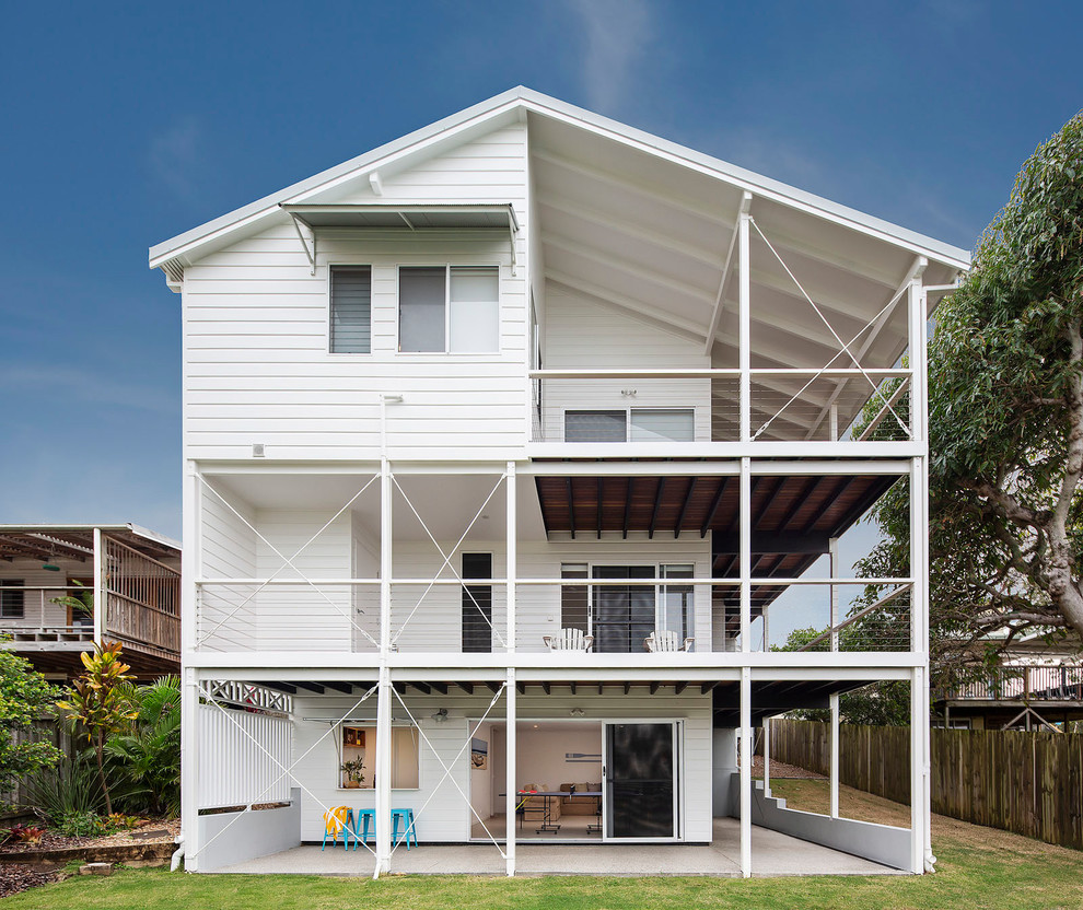Photo of a large beach style three-storey white house exterior in Sunshine Coast with a gable roof, a metal roof and vinyl siding.