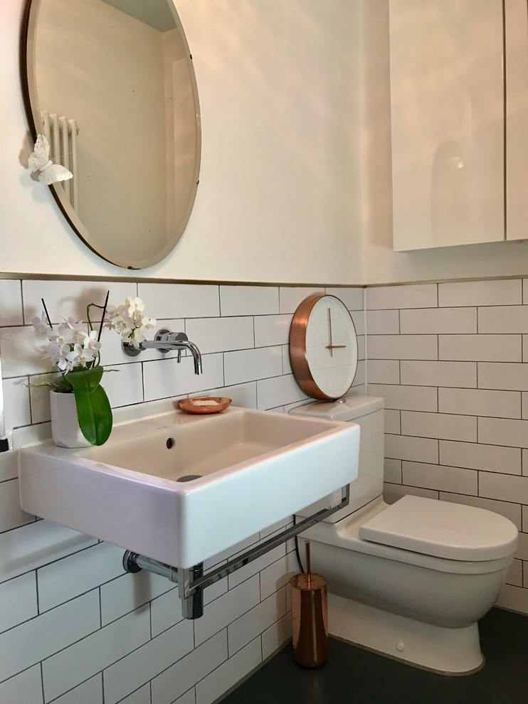 This is an example of a mid-sized modern kids bathroom in London with flat-panel cabinets, white cabinets, a drop-in tub, a shower/bathtub combo, a two-piece toilet, white tile, ceramic tile, white walls, vinyl floors, a wall-mount sink, grey floor, a hinged shower door, a single vanity and a built-in vanity.