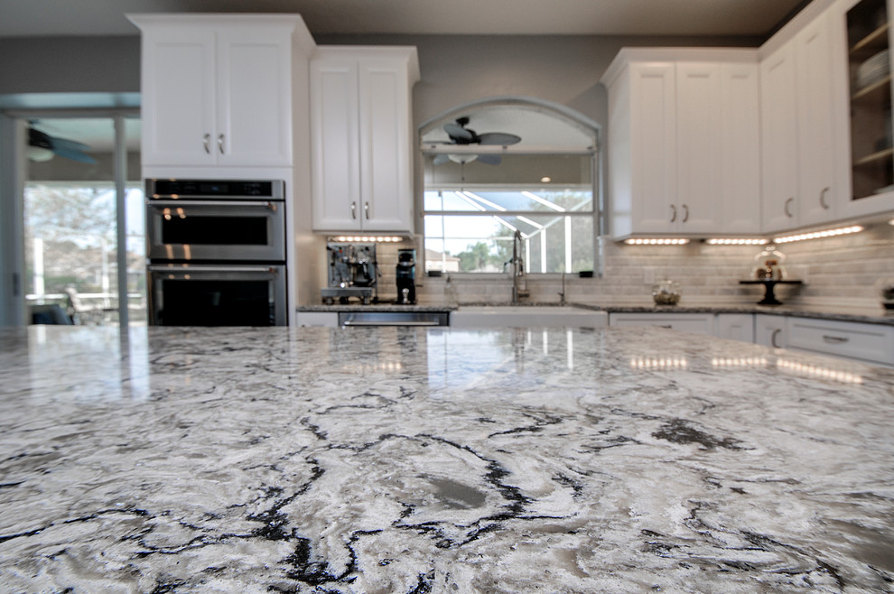 Inspiration for a transitional ceramic tile kitchen remodel in Tampa with a farmhouse sink, white cabinets, white backsplash, stone tile backsplash, stainless steel appliances and an island