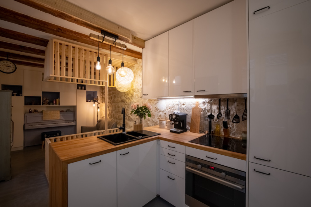 This is an example of a small transitional l-shaped open plan kitchen in Paris with an undermount sink, beaded inset cabinets, white cabinets, wood benchtops, limestone splashback, white appliances, concrete floors, grey floor, brown benchtop and exposed beam.