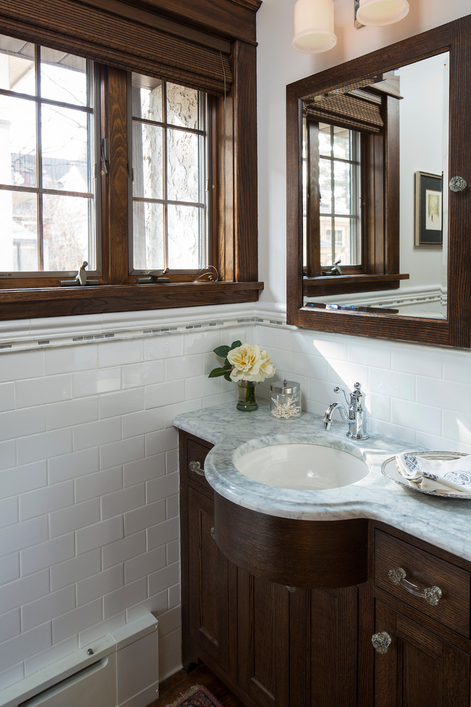 Inspiration for a small traditional powder room in Minneapolis with recessed-panel cabinets, dark wood cabinets, a wall-mount toilet, white tile, subway tile, white walls, medium hardwood floors, an undermount sink, marble benchtops and grey benchtops.