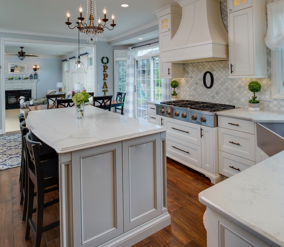 Inspiration for a mid-sized country l-shaped eat-in kitchen in Detroit with a farmhouse sink, recessed-panel cabinets, white cabinets, quartzite benchtops, grey splashback, marble splashback, stainless steel appliances, medium hardwood floors, with island, brown floor and white benchtop.