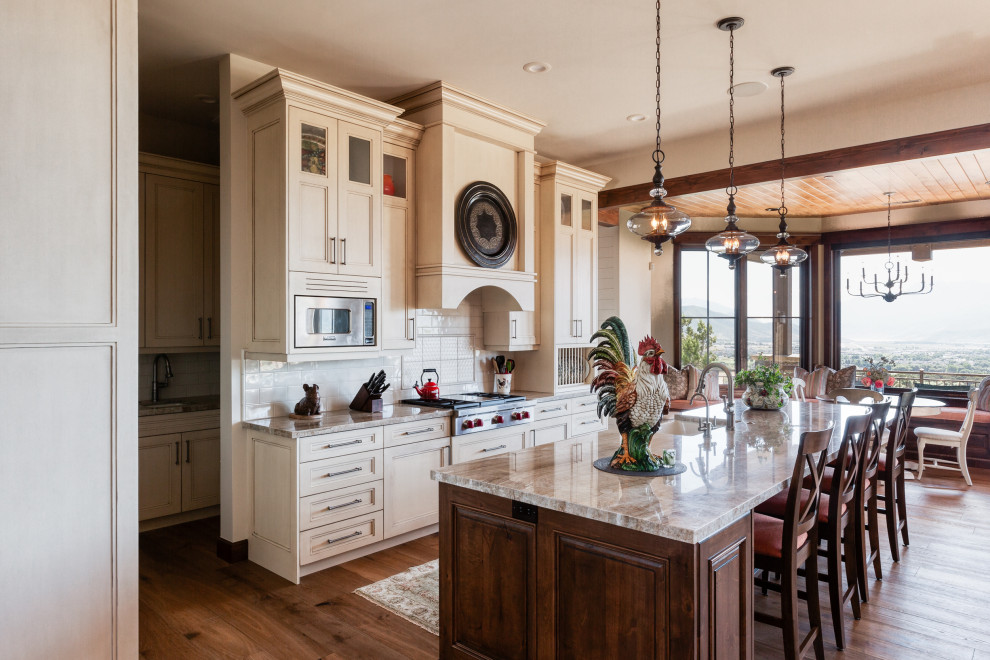 Inspiration for a traditional galley kitchen in Salt Lake City with a farmhouse sink, recessed-panel cabinets, beige cabinets, white splashback, stainless steel appliances, dark hardwood floors, with island, brown floor and brown benchtop.