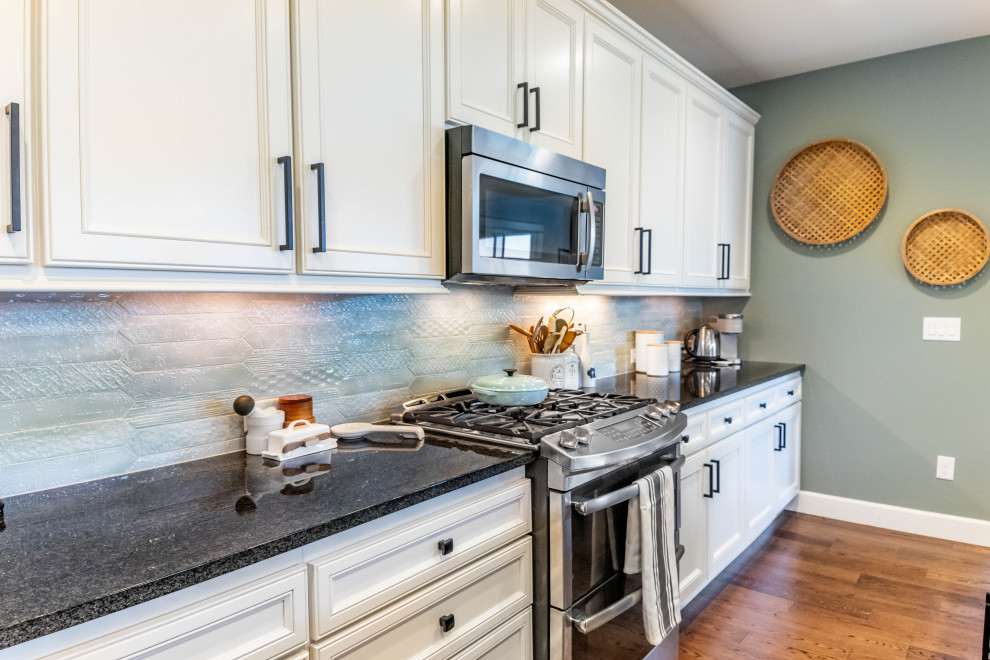 Example of a mid-sized beach style single-wall medium tone wood floor and brown floor open concept kitchen design in Seattle with an undermount sink, beaded inset cabinets, white cabinets, granite countertops, green backsplash, ceramic backsplash, stainless steel appliances, an island and gray countertops