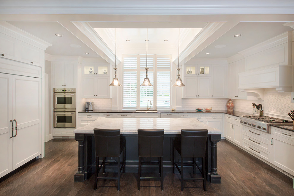 Inspiration for a transitional u-shaped dark wood floor eat-in kitchen remodel in Omaha with an undermount sink, recessed-panel cabinets, white cabinets, granite countertops, white backsplash, porcelain backsplash, paneled appliances and an island