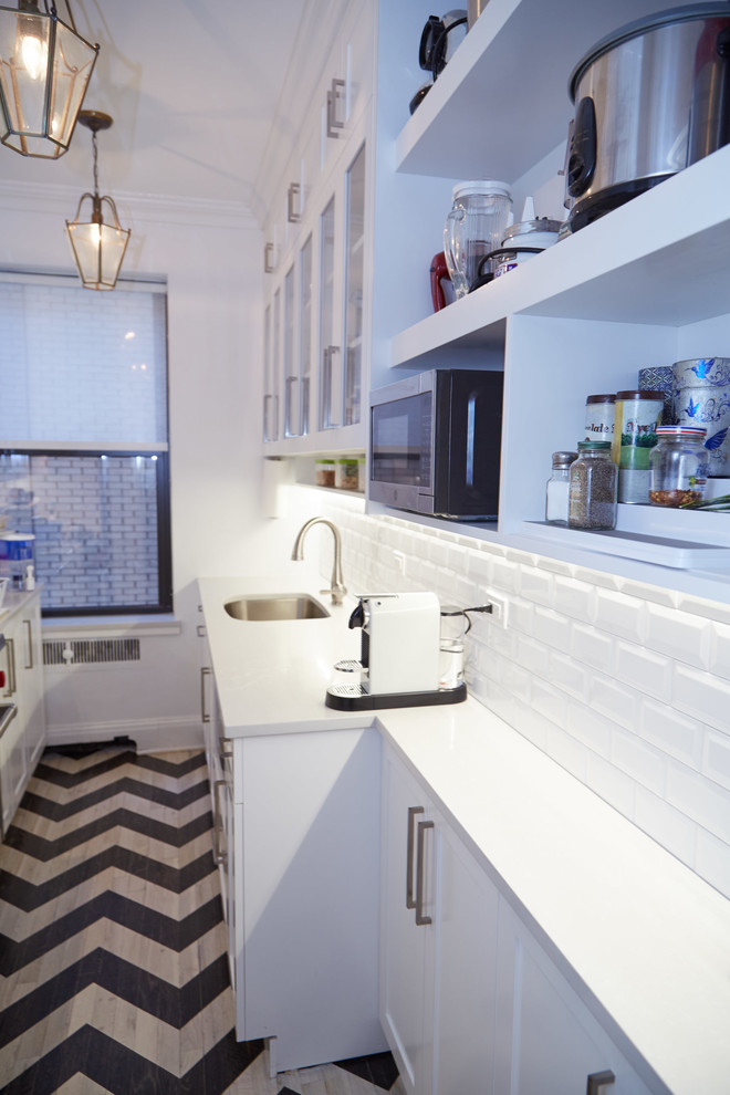 Photo of a small contemporary galley separate kitchen in New York with shaker cabinets, white cabinets, white splashback, stainless steel appliances, painted wood floors and no island.