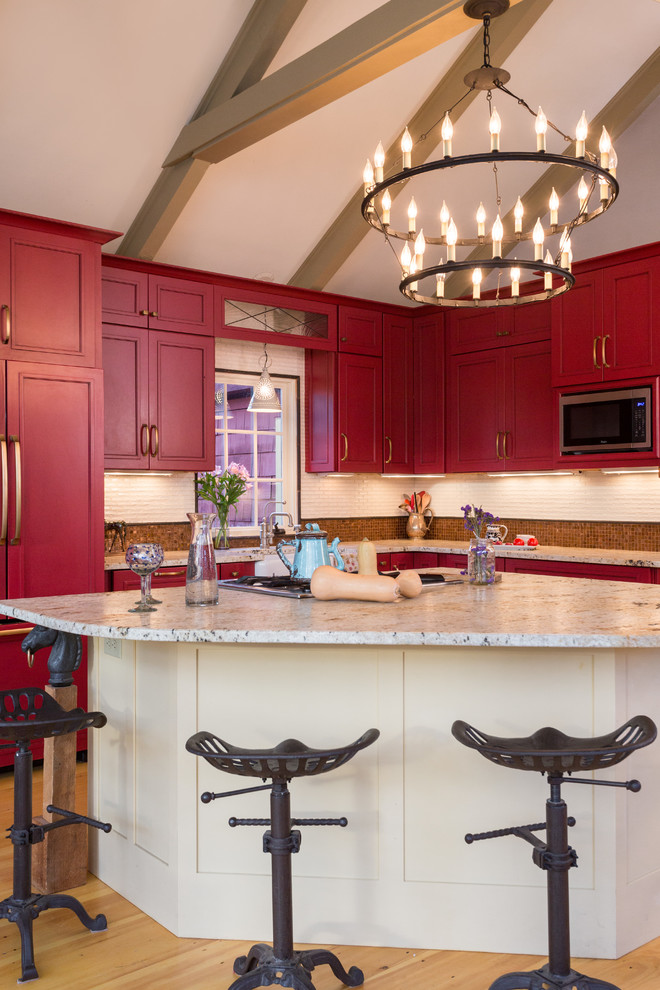 This is an example of a mid-sized country l-shaped eat-in kitchen in Boston with shaker cabinets, red cabinets, granite benchtops, beige splashback, stone slab splashback, stainless steel appliances, medium hardwood floors, with island and beige floor.