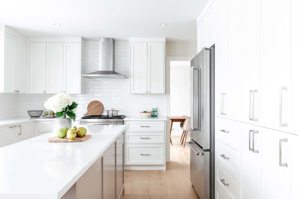 Inspiration for a large transitional u-shaped medium tone wood floor and brown floor eat-in kitchen remodel in Calgary with an undermount sink, shaker cabinets, white cabinets, quartzite countertops, white backsplash, subway tile backsplash, stainless steel appliances, an island and white countertops