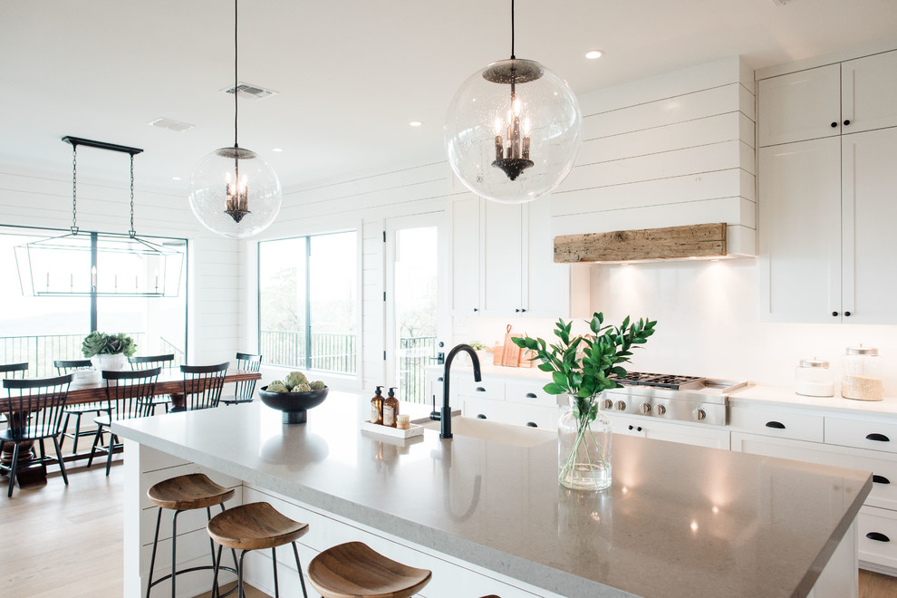 Inspiration for a large transitional u-shaped open plan kitchen in Austin with a farmhouse sink, shaker cabinets, white cabinets, quartzite benchtops, white splashback, stone slab splashback, stainless steel appliances, light hardwood floors, with island, brown floor and grey benchtop.