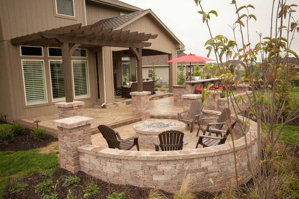This is an example of a modern backyard patio in Kansas City with an outdoor kitchen, stamped concrete and a pergola.