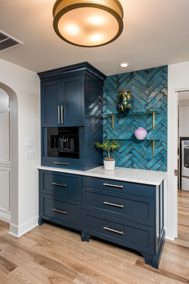 Photo of a large traditional single-wall home bar in Other with shaker cabinets, blue cabinets, marble benchtops, blue splashback, ceramic splashback, light hardwood floors and white benchtop.