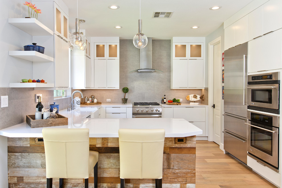 Design ideas for a mid-sized transitional u-shaped open plan kitchen in Tampa with a farmhouse sink, flat-panel cabinets, white cabinets, quartz benchtops, grey splashback, porcelain splashback, stainless steel appliances, light hardwood floors, a peninsula and beige floor.