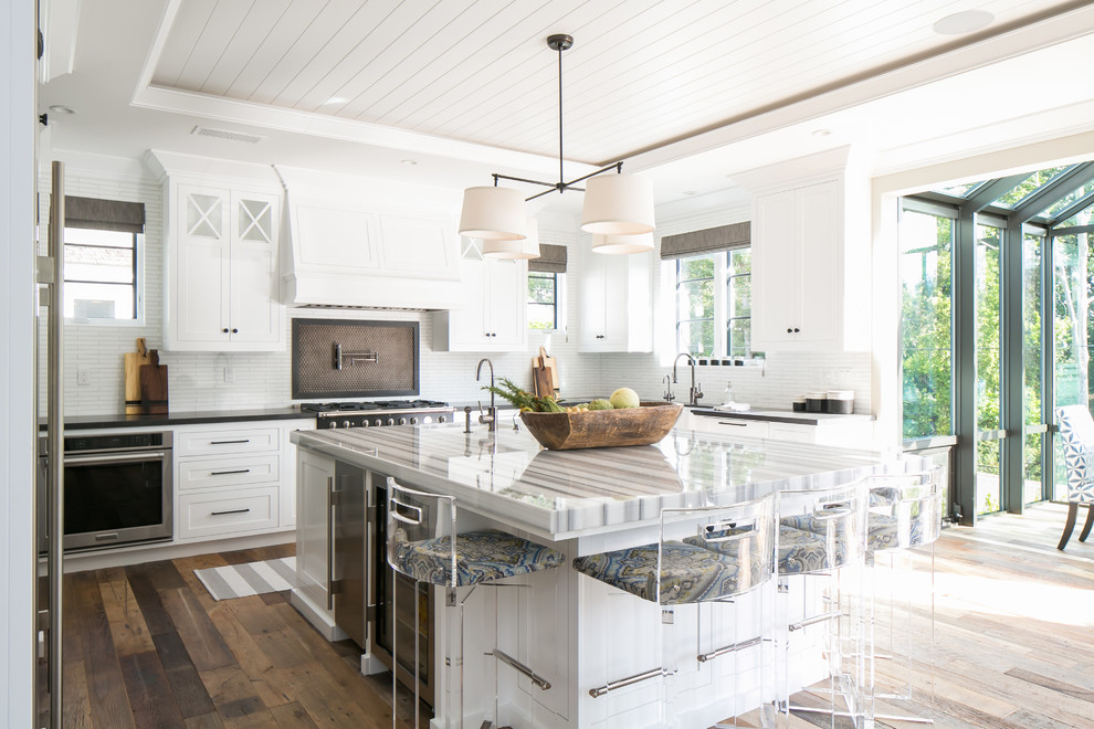 Beach style u-shaped kitchen in Orange County with shaker cabinets, white cabinets, white splashback, stainless steel appliances, dark hardwood floors and with island.
