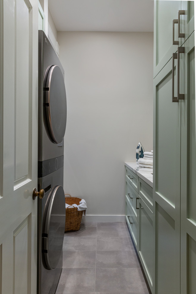Example of a small transitional galley porcelain tile and gray floor dedicated laundry room design in San Francisco with an utility sink, shaker cabinets, green cabinets, quartz countertops, green backsplash, porcelain backsplash, beige walls, a stacked washer/dryer and white countertops