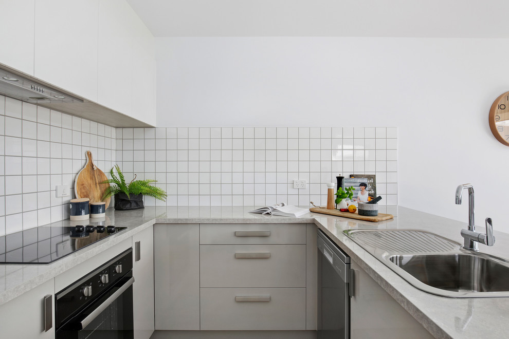 Inspiration for a small contemporary u-shaped open plan kitchen in Other with a drop-in sink, grey cabinets, laminate benchtops, white splashback, ceramic splashback, black appliances, vinyl floors, no island, brown floor and grey benchtop.