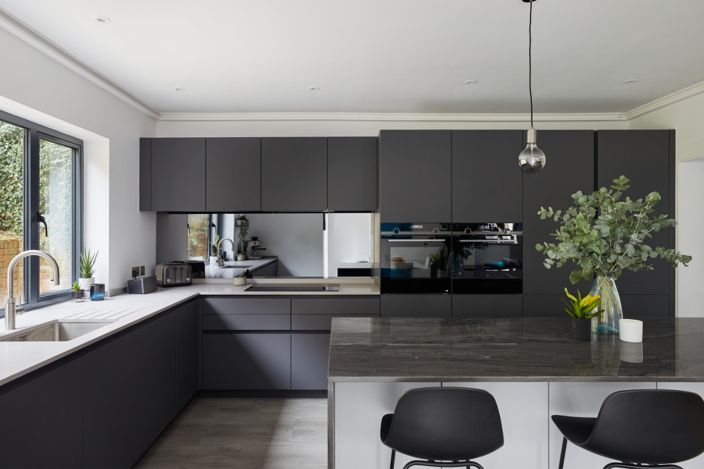 Photo of a medium sized contemporary l-shaped kitchen/diner in London with a submerged sink, flat-panel cabinets, grey cabinets, glass sheet splashback, stainless steel appliances and an island.