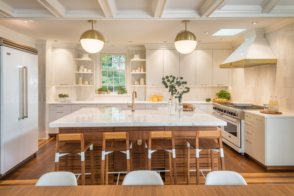 Design ideas for a large contemporary u-shaped eat-in kitchen in New York with a farmhouse sink, flat-panel cabinets, white cabinets, marble benchtops, white splashback, subway tile splashback, white appliances, medium hardwood floors, with island, brown floor and white benchtop.