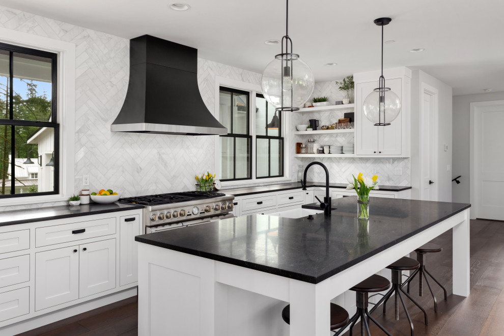 Large contemporary u-shaped eat-in kitchen in San Francisco with shaker cabinets, white cabinets, quartz benchtops, white splashback, marble splashback, black appliances, laminate floors, with island, brown floor and black benchtop.