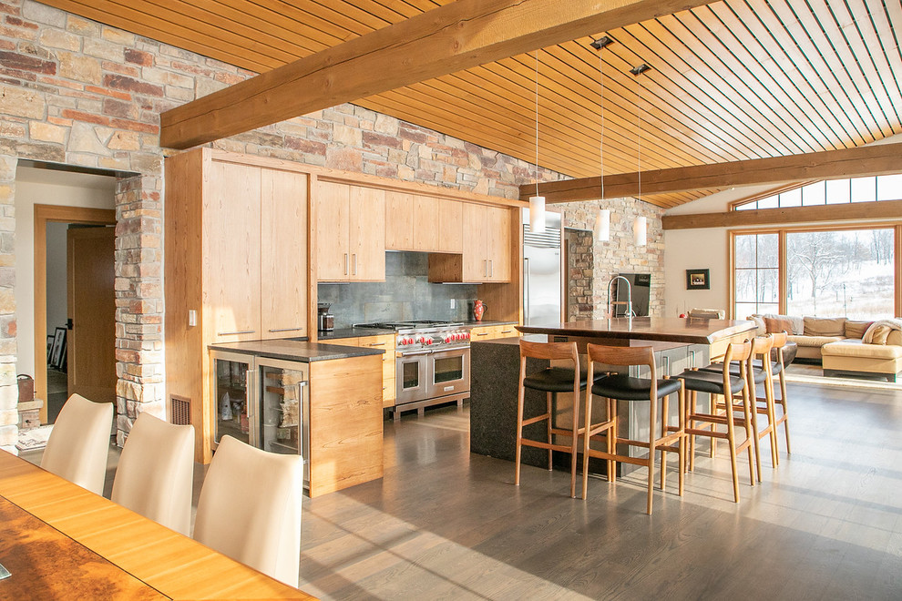 Inspiration for a large rustic l-shaped medium tone wood floor and brown floor open concept kitchen remodel with a double-bowl sink, flat-panel cabinets, light wood cabinets, granite countertops, black backsplash, stainless steel appliances, an island, black countertops and porcelain backsplash