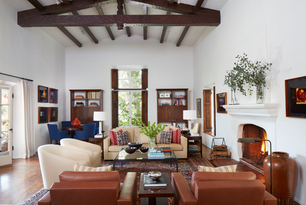 Inspiration for a large mediterranean open concept living room in Los Angeles with white walls, dark hardwood floors, a plaster fireplace surround and a concealed tv.