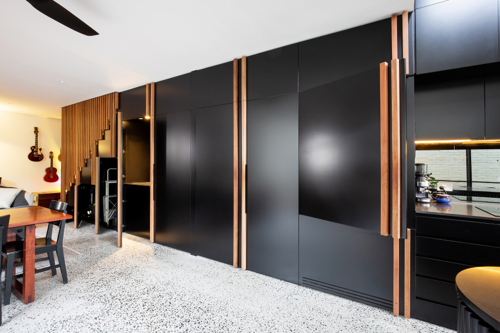 Design ideas for a mid-sized contemporary single-wall kitchen in Other with a drop-in sink, shaker cabinets, black cabinets, quartz benchtops, black splashback, mirror splashback, black appliances, terrazzo floors, with island, grey floor and black benchtop.