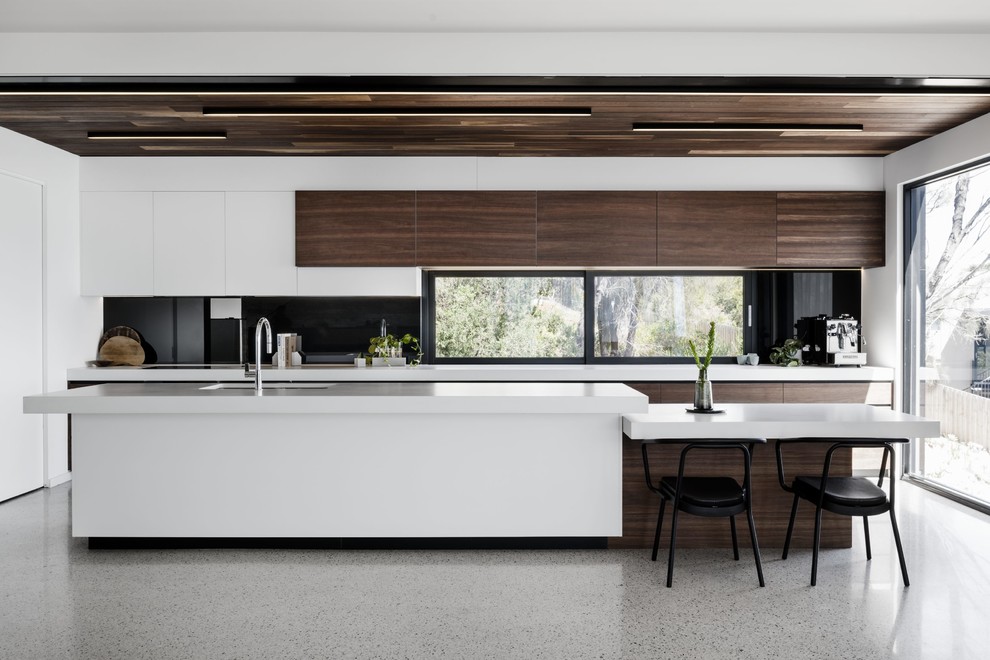 This is an example of a contemporary galley open plan kitchen in Melbourne with an undermount sink, flat-panel cabinets, dark wood cabinets, black splashback, window splashback, coloured appliances, with island, grey floor and white benchtop.