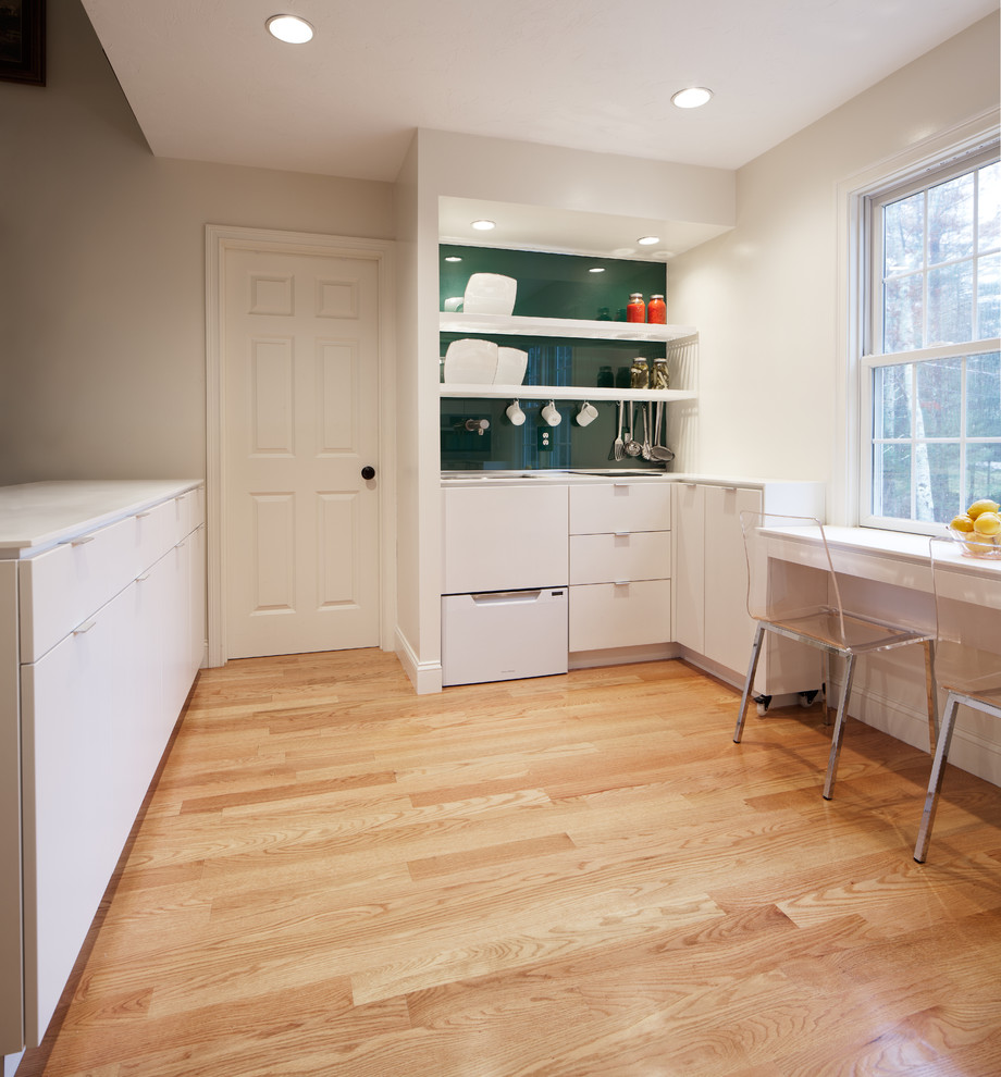 This is an example of a contemporary u-shaped eat-in kitchen in Boston with an undermount sink, flat-panel cabinets, white cabinets, solid surface benchtops, green splashback, glass sheet splashback and stainless steel appliances.