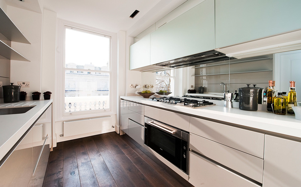This is an example of a small contemporary galley separate kitchen in London with a drop-in sink, flat-panel cabinets, white cabinets, quartzite benchtops, metallic splashback, mirror splashback, stainless steel appliances, dark hardwood floors and no island.