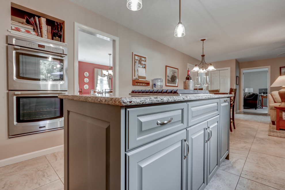 Example of a mid-sized transitional l-shaped ceramic tile and beige floor eat-in kitchen design with a double-bowl sink, raised-panel cabinets, green cabinets, granite countertops, beige backsplash, ceramic backsplash, stainless steel appliances, an island and beige countertops