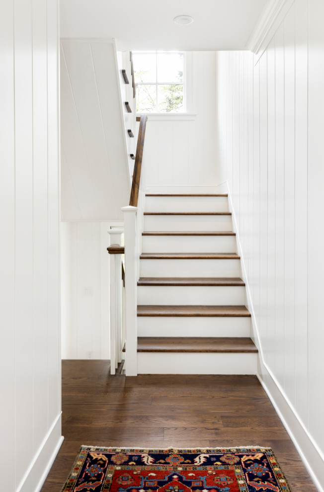 ポートランドにある高級なトラディショナルスタイルのおしゃれな階段 (フローリングの蹴込み板、木材の手すり、塗装板張りの壁) の写真