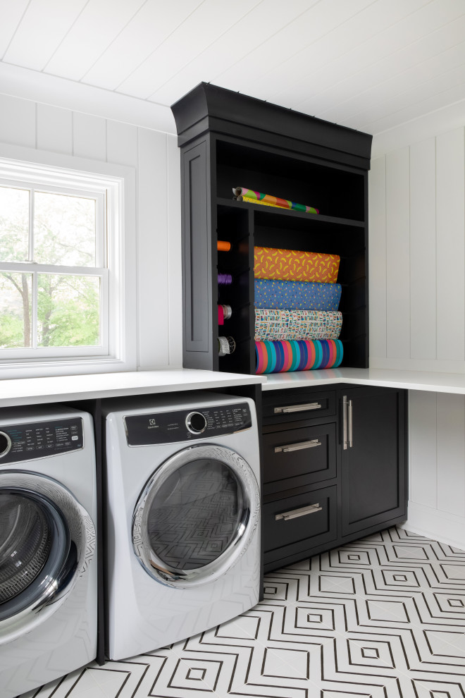 Photo of an expansive transitional l-shaped utility room in New York with an integrated sink, beaded inset cabinets, black cabinets, quartz benchtops, white splashback, shiplap splashback, white walls, ceramic floors, a side-by-side washer and dryer, multi-coloured floor, white benchtop, timber and planked wall panelling.