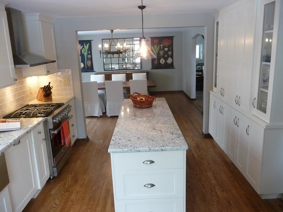 Large transitional u-shaped light wood floor home design photo in Milwaukee with a farmhouse sink, recessed-panel cabinets, white cabinets, granite countertops, gray backsplash, subway tile backsplash, stainless steel appliances and an island