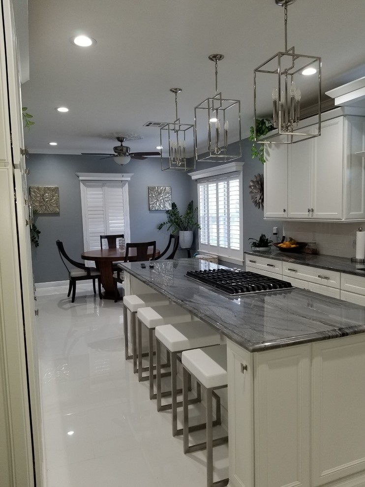 Design ideas for a large contemporary l-shaped eat-in kitchen in New Orleans with an undermount sink, recessed-panel cabinets, white cabinets, quartzite benchtops, white splashback, porcelain splashback, stainless steel appliances, porcelain floors, with island, white floor and blue benchtop.