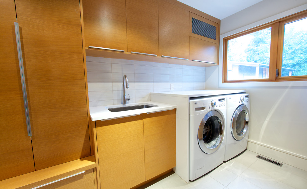 Photo of a large contemporary galley dedicated laundry room in Vancouver with an undermount sink, flat-panel cabinets, white walls, ceramic floors, a side-by-side washer and dryer and medium wood cabinets.
