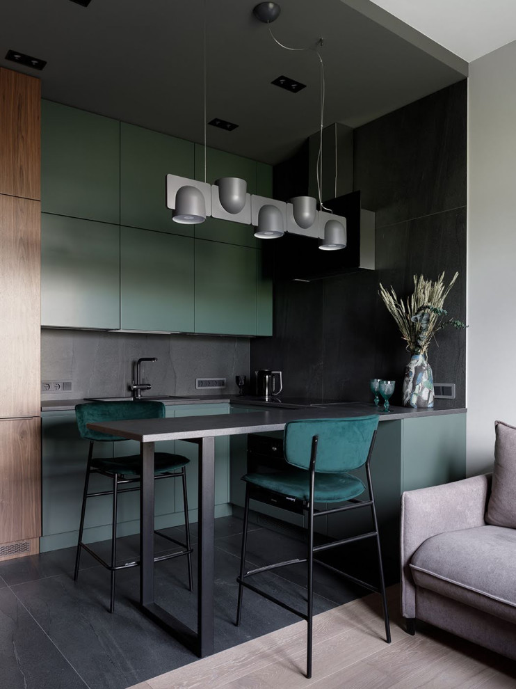 На фото: угловая кухня-гостиная в современном стиле с плоскими фасадами, зелеными фасадами, серым фартуком, серым полом, серой столешницей и барной стойкой