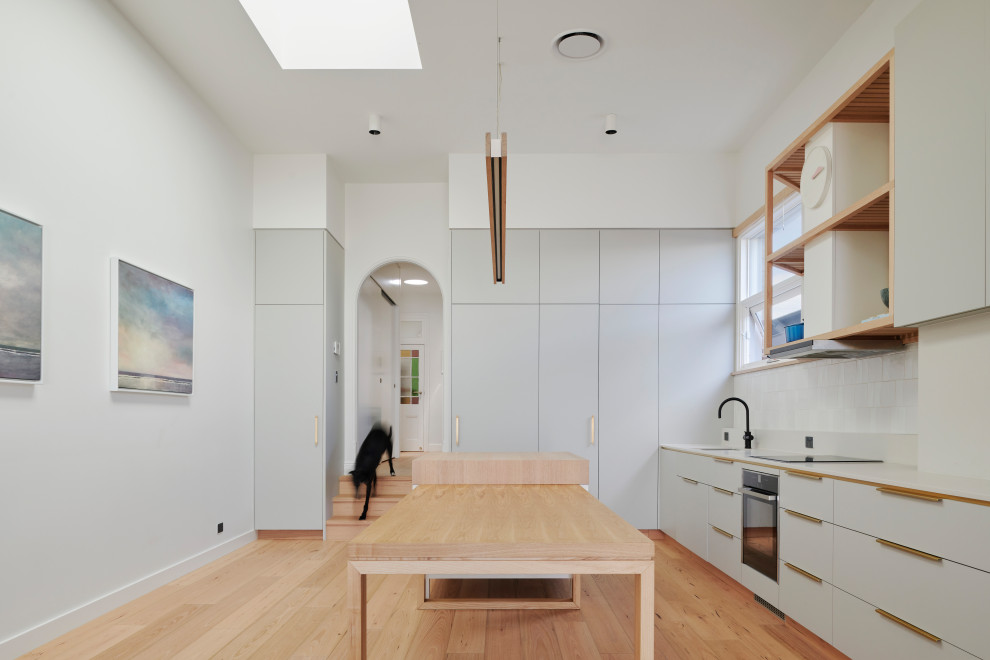 This is an example of a large contemporary l-shaped eat-in kitchen in Sydney with an undermount sink, flat-panel cabinets, grey cabinets, quartz benchtops, white splashback, ceramic splashback, light hardwood floors, with island and grey benchtop.