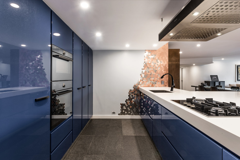 Photo of a large contemporary galley eat-in kitchen in Sydney with an integrated sink, flat-panel cabinets, blue cabinets, solid surface benchtops, metallic splashback, metal splashback, black appliances, light hardwood floors, with island and brown floor.
