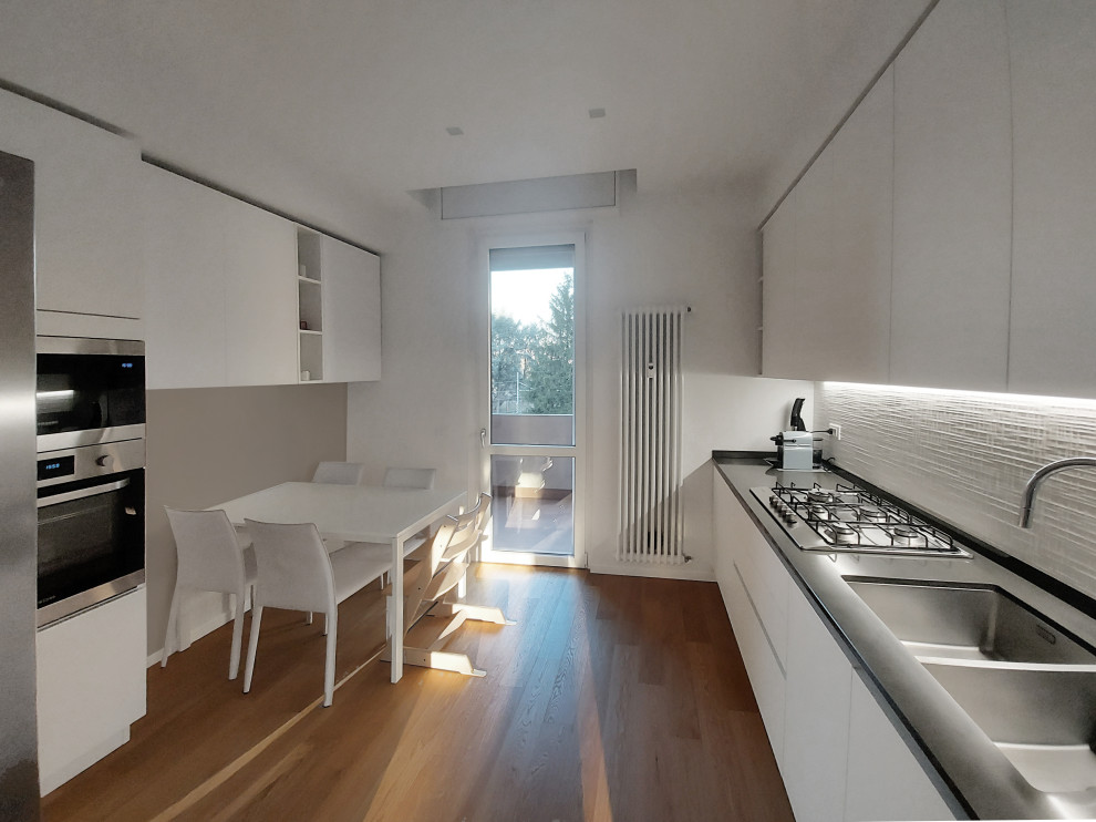 Design ideas for a mid-sized contemporary galley separate kitchen in Milan with a drop-in sink, flat-panel cabinets, white cabinets, quartzite benchtops, white splashback, porcelain splashback, light hardwood floors, black benchtop and recessed.