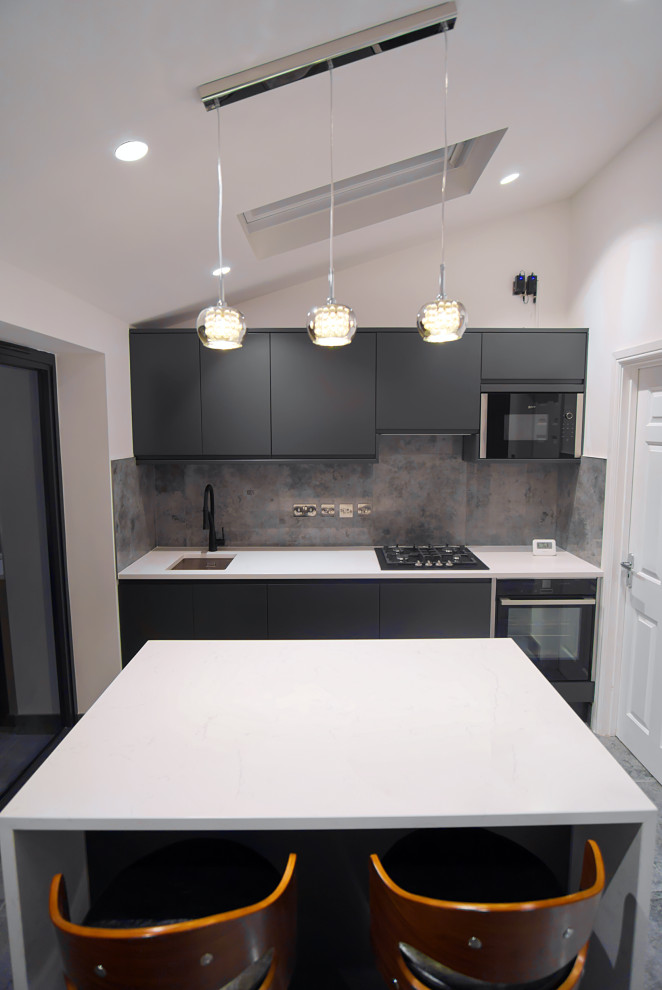 Inspiration for a small modern grey and black l-shaped kitchen/diner in London with an integrated sink, flat-panel cabinets, grey cabinets, grey splashback, porcelain splashback, black appliances, porcelain flooring, an island, grey floors, white worktops, feature lighting, quartz worktops and a drop ceiling.
