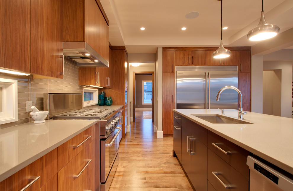 Trendy medium tone wood floor kitchen photo in Other with an undermount sink, flat-panel cabinets, medium tone wood cabinets, quartzite countertops, gray backsplash, glass tile backsplash, stainless steel appliances and an island